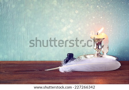 low key image of white Feather, inkwell, scroll and  glitter lights background on old wooden table