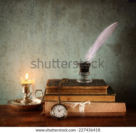 low key image of white Feather, inkwell, candle and old books on  wooden table. image filtered and  textured