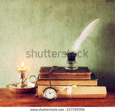 low key image of white Feather, inkwell and ancient books on old wooden table. image textured
