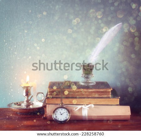 low key image of white Feather, inkwell, old books and candle and glitter lights background on old wooden table