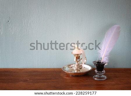 low key image of white Feather, inkwell, and candle on old wooden table. filtered image
