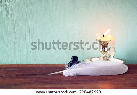 low key image of white Feather, inkwell and candle on old wooden table