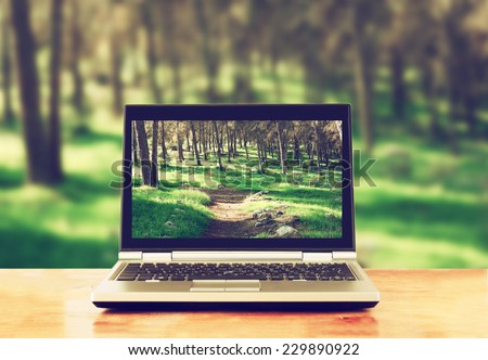 laptop over wooden table outdoors and blurred background of trees in the forest