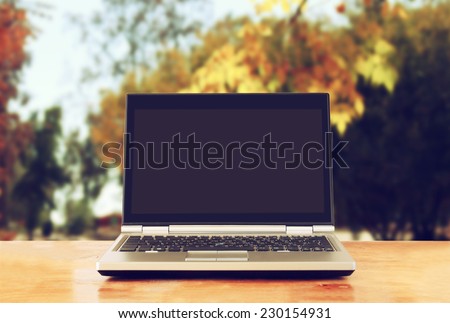 laptop with blank screen over wooden table outdoors and blurred background of trees in the forest