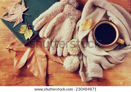 Top view of Cup of black coffee with autumn leaves, a warm scarf and old book on wooden background. filtered image