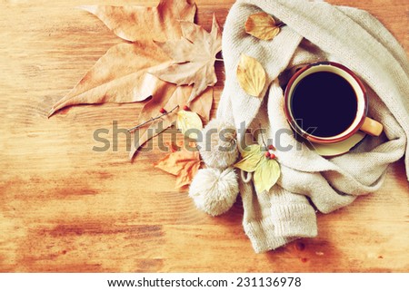 Cup of black coffee with autumn leaves, a warm scarf and old book on wooden background.