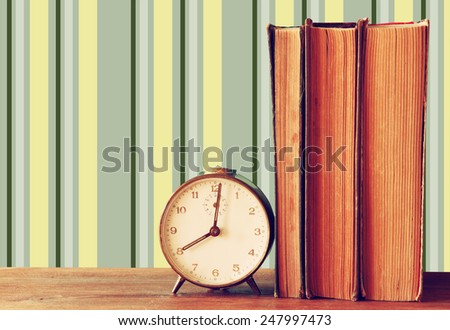 stack of old books and old clock over wooden table and retro style wallpaper