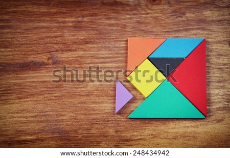 top view of a missing piece in a square tangram puzzle, over wooden table.