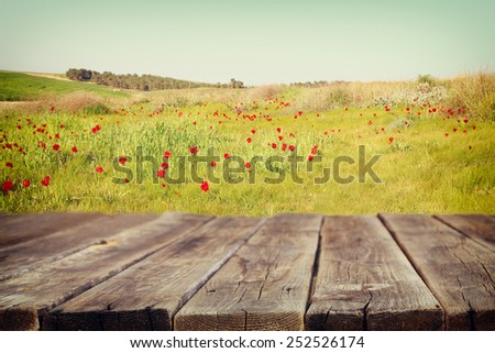 wood board table in front of summer landscape of field with many flowers . background is blurred