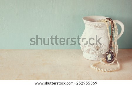 white classic victorian vase on wooden table with a collection of romantic vintage jewelry and pearls. retro filtered image. room for text