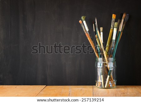paint brushes in jar over blackboard background