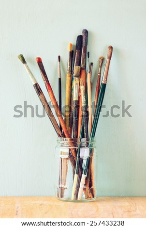 paint brushes in jar over wooden aqua blue background. vintage filtered image