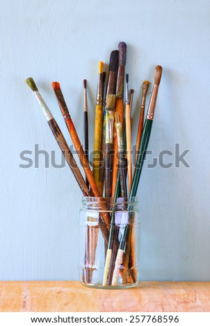 paint brushes in jar over wooden aqua blue background