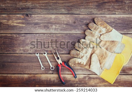 top view of worn work gloves and assorted work tools over wooden background