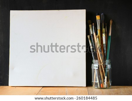 paint brushes in jar and blank canvas over blackboard background