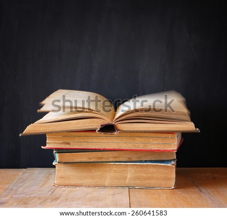 stack of old books, top book is open and pages are in motion, over wooden table and wooden background