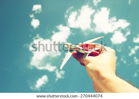 close up photo of man\'s hand holding toy airplane against blue sky with clouds. filtered image