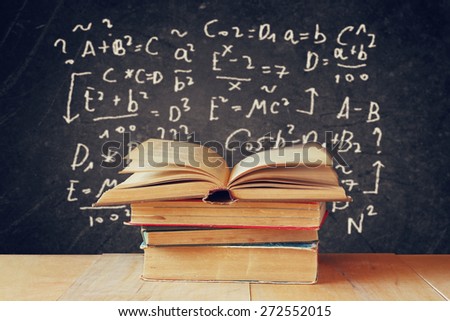 image of school books on wooden desk over black background with formulas. education concept