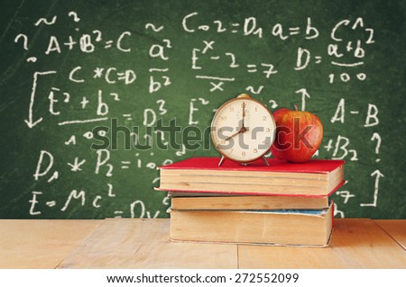 image of school books on wooden desk, apple and vintage clock over green background with formulas. education concept
