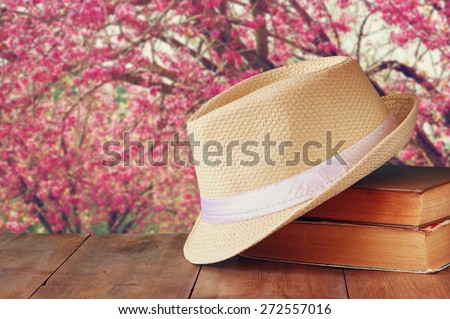 fedora hat and stack of books over wooden table and cherry blossom tree landscape background. relaxation or vacation concept