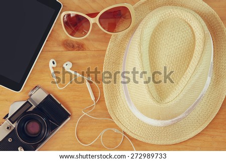 top view of stylish hat woman sunglasses old camera and tablet device over wooden table. vaction and travel concept