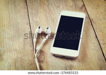 Top view of white phone and earphones on wooden table