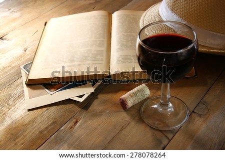 Red wine glass and old open book on wooden table at sun burst. vintage filtered image