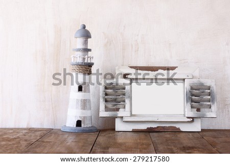 Old vintage wooden white frame and lighthouse on wooden table. vintage filtered image. nautical lifestyle concept
