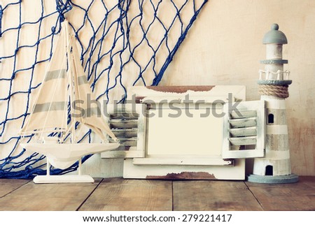 old vintage wooden white frame, lighthouse and sailing boat on wooden table. vintage filtered image. nautical lifestyle concept