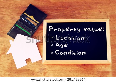 top view of blackboard with the phrase property value, open wallet and paper house shape