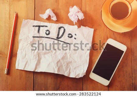 top view image of blank paper with the text to do in hand write, next to cellphone and coffee cup over wooden table