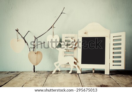 abstract filtered photo of decorative chalkboard frame and wooden hanging hearts over wooden table. ready for text or mockup