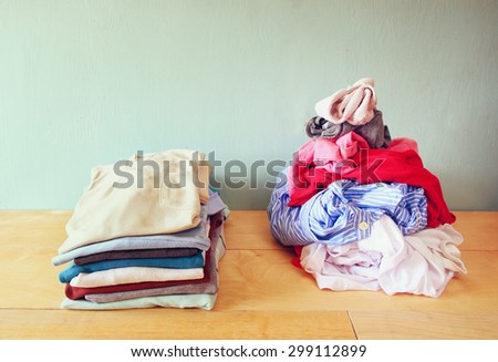 Pile of unfolded clothes next to stack of clean folded laundry over wooden table