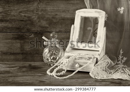vintage pearls , antique wooden jewelry box with mirror and perfume bottle on wooden table. black and white style photo