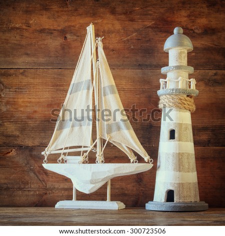 old vintage wooden lighthouse and sailing boat on wooden table. vintage filtered image. nautical lifestyle concept