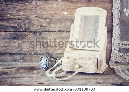 vintage pearls , antique wooden jewelry box with mirror and perfume bottle on wooden table. filtered image with glitter overlay