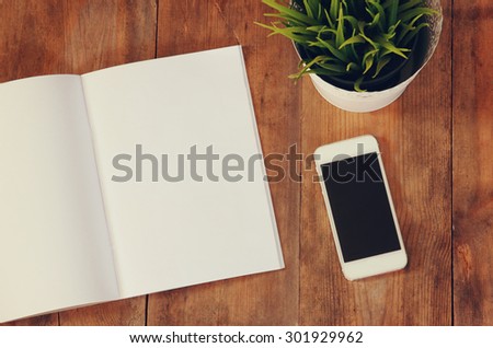 top view image of open notebook with blank pages next to smartphone  on wooden table. ready for adding text or mockup