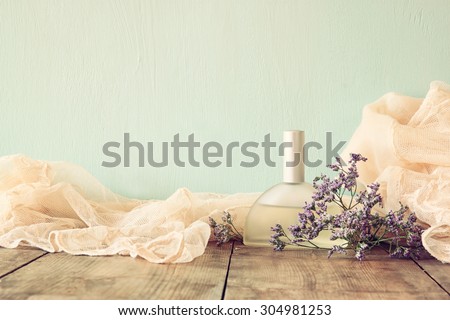 fresh vintage perfume bottle next to aromatic flowers on wooden table. retro filtered image