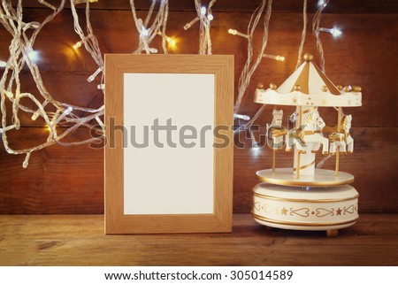 abstract image of old vintage white carousel horses with garland gold lights and blank frame on wooden table. retro filtered image