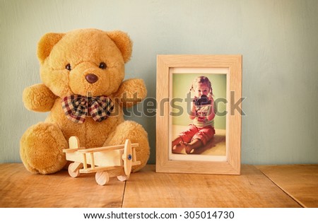 wooden airplane toy and teddy bear over wood table next to photo frame with kid\'s old photography. retro filtered image