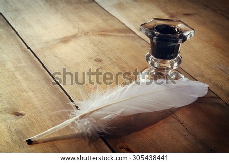 photo of white Feather and inkwell on old wooden table