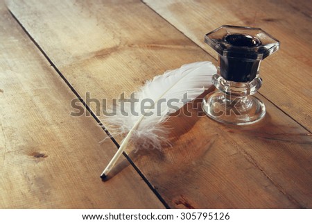 photo of white Feather and inkwell on old wooden table