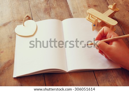 open blank notebook and woman hands next to toy aeroplane on wooden table. retro style  filtered image