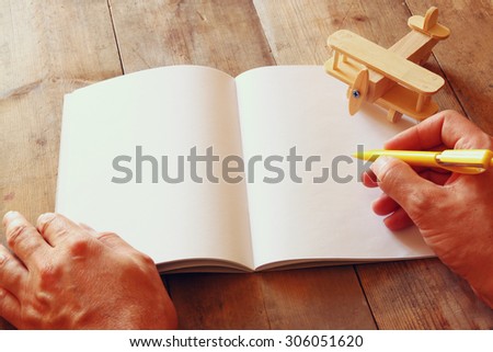 open blank notebook and man hands next to toy aeroplane on wooden table. retro style filtered image