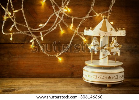 old vintage white carousel horses with garland gold lights on wooden table. retro filtered image