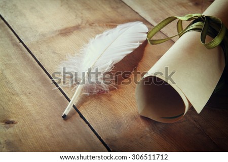 photo of white Feather and scroll paper on old wooden table. retro filtered image