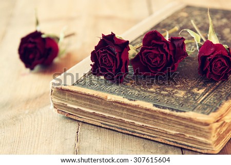 selective focus image of dry red roses and old vintage books on wooden table. retro filtered image