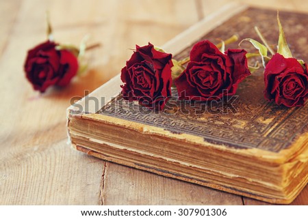 selective focus image of dry red roses and old vintage books on wooden table. retro filtered image