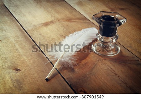 photo of white Feather and inkwell on old wooden table. retro filtered image