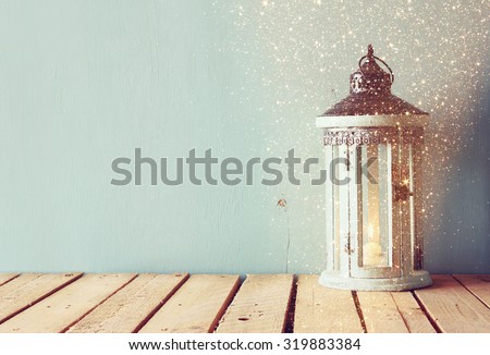 white wooden vintage lantern with burning candle and tree branches on wooden table. retro filtered image with glitter overlay